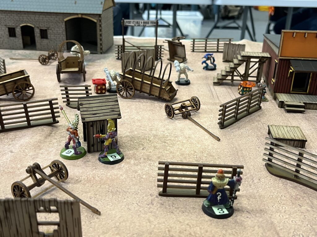 The left hand side of the tabletop. There are 3 crew miniatures in sight representing Starburn, Doc and Wolf. There is an array of Gang miniatures in front of them. Everyone is in cover. Gimmet Y appears in the background traversing the table to the left.
