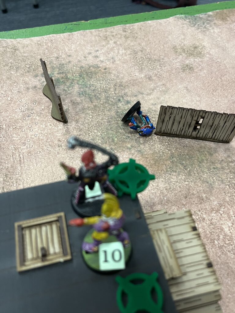 An above angle shot of 2 miniatures on top of a building and one lying on down on the table. The scene shows the death of Gimmet Y, who was shot from above.